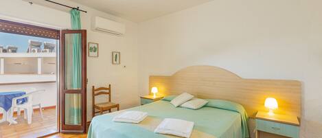 A bedroom with a bed, two bedside tables with lamps, a chair, a table, and a balcony with a view.