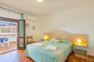 A bedroom with a bed, two bedside tables with lamps, a chair, a table, and a balcony with a view.