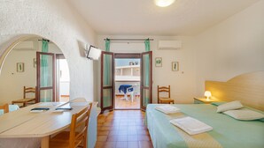 A room with a bed, a desk, chairs, a TV, and a view through an open door. - Hotel Mare Blue (Olbia)