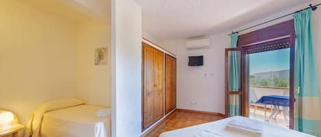 Ein Hotelzimmer mit zwei Einzelbetten, einem kleinen Tisch mit Lampe, einem Fernseher und einer Glasschiebetür zu einem Außenbereich mit Tisch und Stühlen.