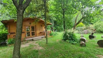 A wooden cabin with a porch, surrounded by lush greenery and trees.