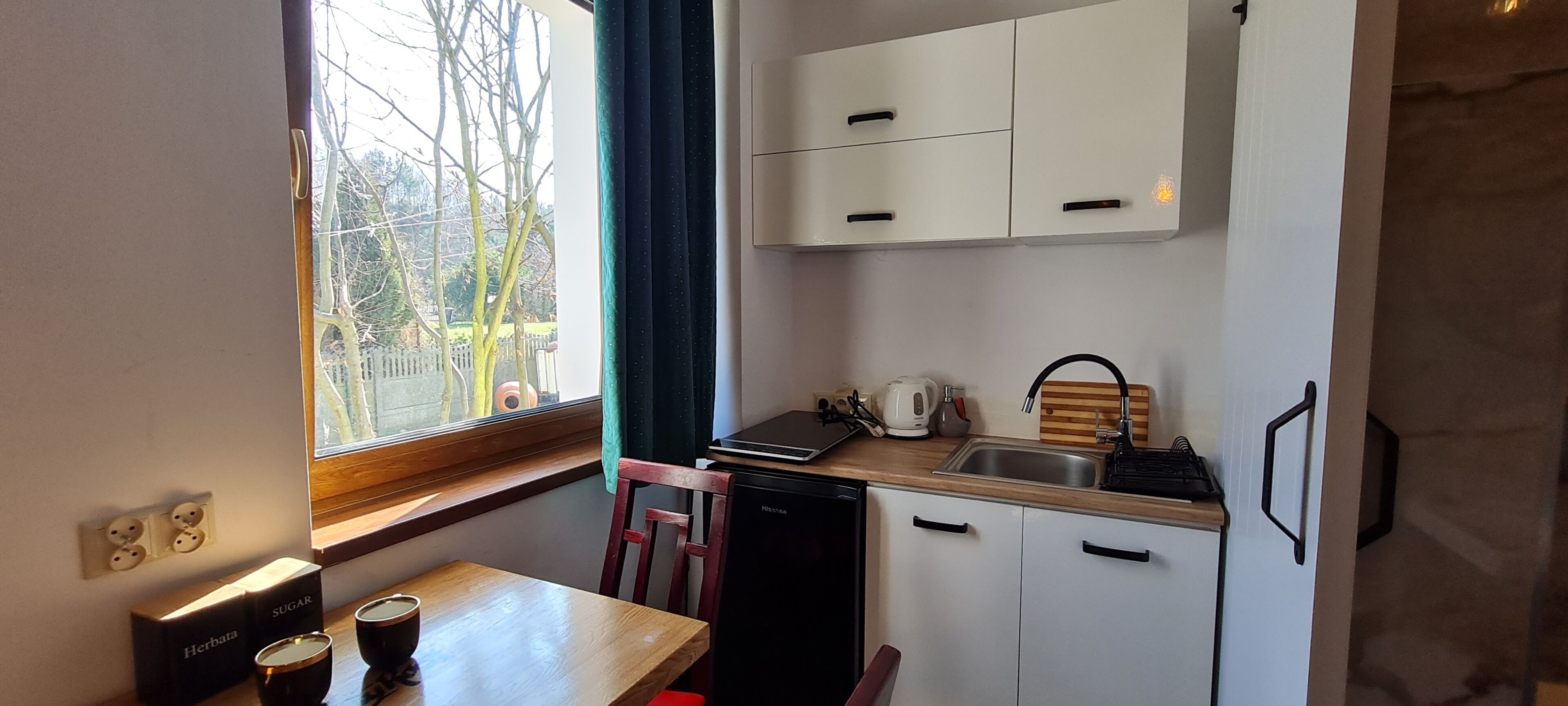 A compact kitchen with a window, a sink, a refrigerator, and a dining area with a table and chairs.