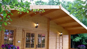 Une cabane en bois dotée d’un porche abrité, de grandes fenêtres et d’une table avec des chaises.