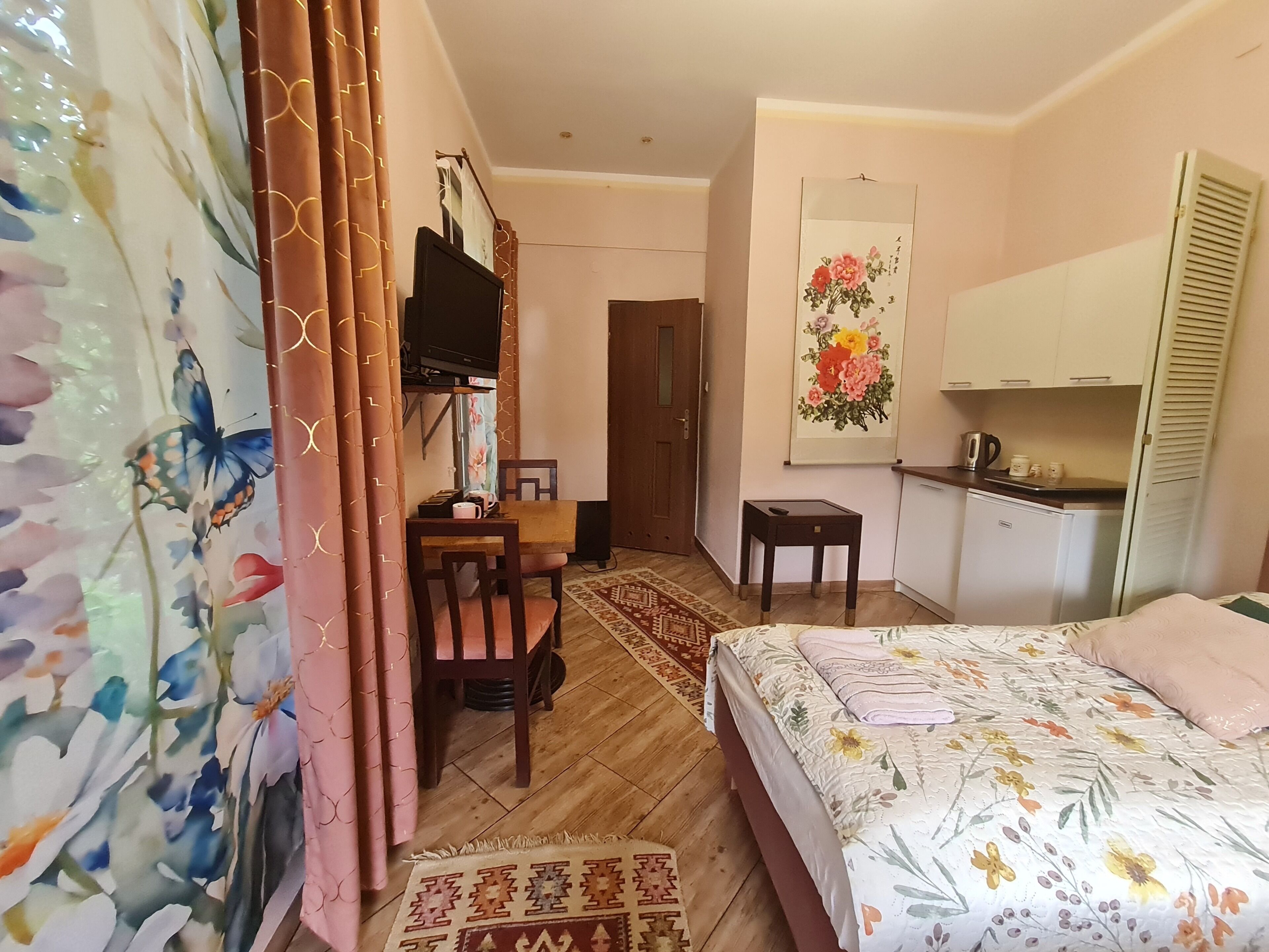 Un dormitorio con cama, escritorio, silla, televisión y zona de cocina.