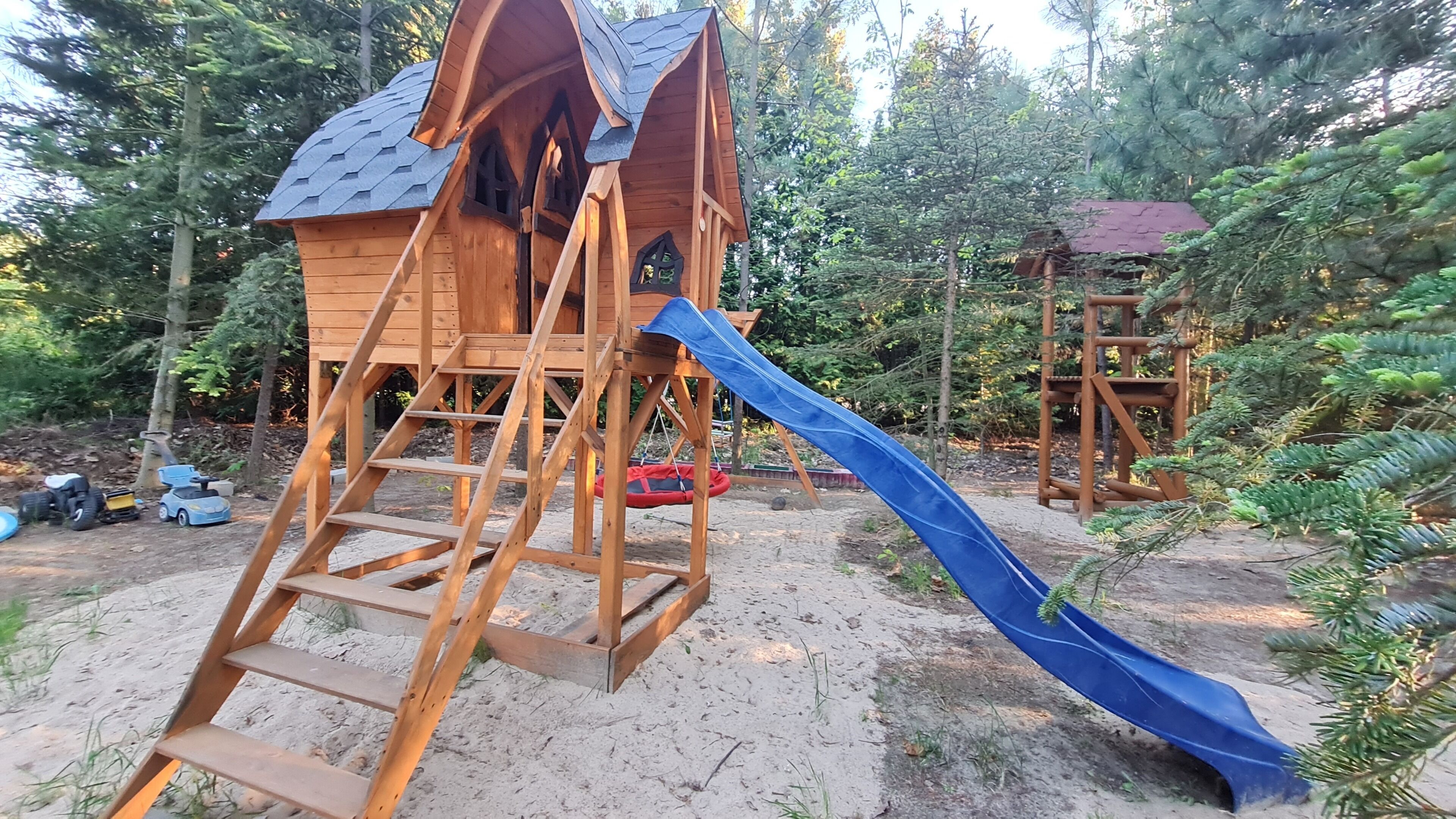 A wooden playhouse with a slide, surrounded by trees.