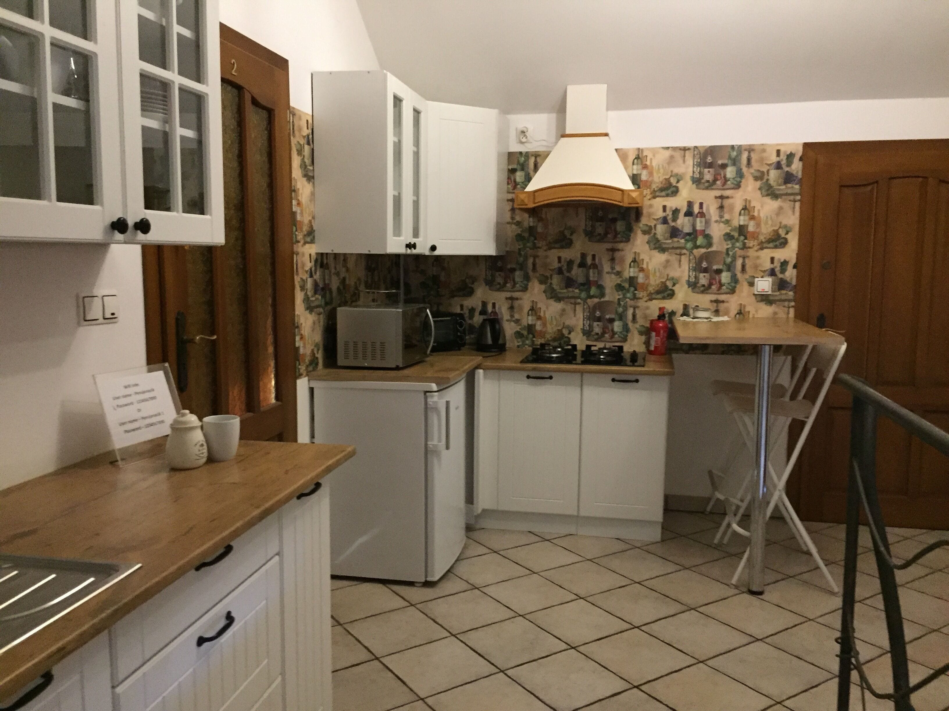 Eine kompakte Küche mit weißen Schränken, einer Mikrowelle, einem kleinen Kühlschrank, einem Gasherd und einer Holz Arbeitsplatte.