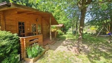A wooden cabin with a porch, a garden with plants, and a swing set.