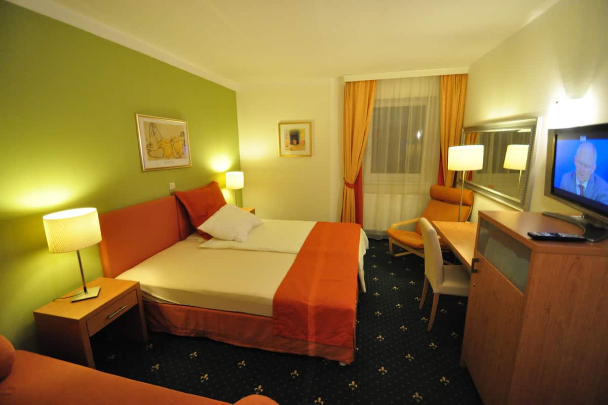 A hotel room with a bed, a desk, a chair, a TV, and two lamps.