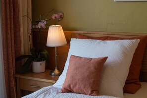 A neatly made bed with white and brown pillows, a bedside lamp, and a potted plant on a wooden nightstand. - Landgasthof Hotel Kreuzwirt (Engerwitzdorf)