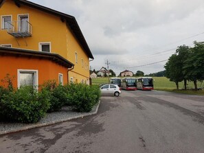 A yellow building with a balcony, a car, and buses parked in front. - Landgasthof Hotel Kreuzwirt (Engerwitzdorf)