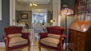 A room with two red upholstered chairs with striped cushions, a wooden bookcase, and a chandelier. - Avoca House (Dublin)