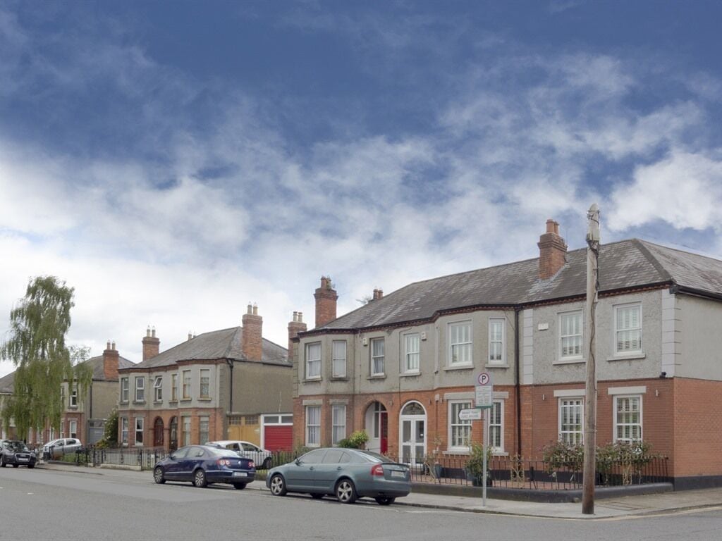 A residential street with houses, parked cars, and a clear sky.