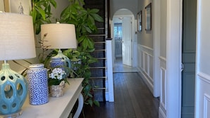 A hallway with a wooden floor, a white console table with decorative items, a staircase, and a door at the end. - Avoca House (Dublin)