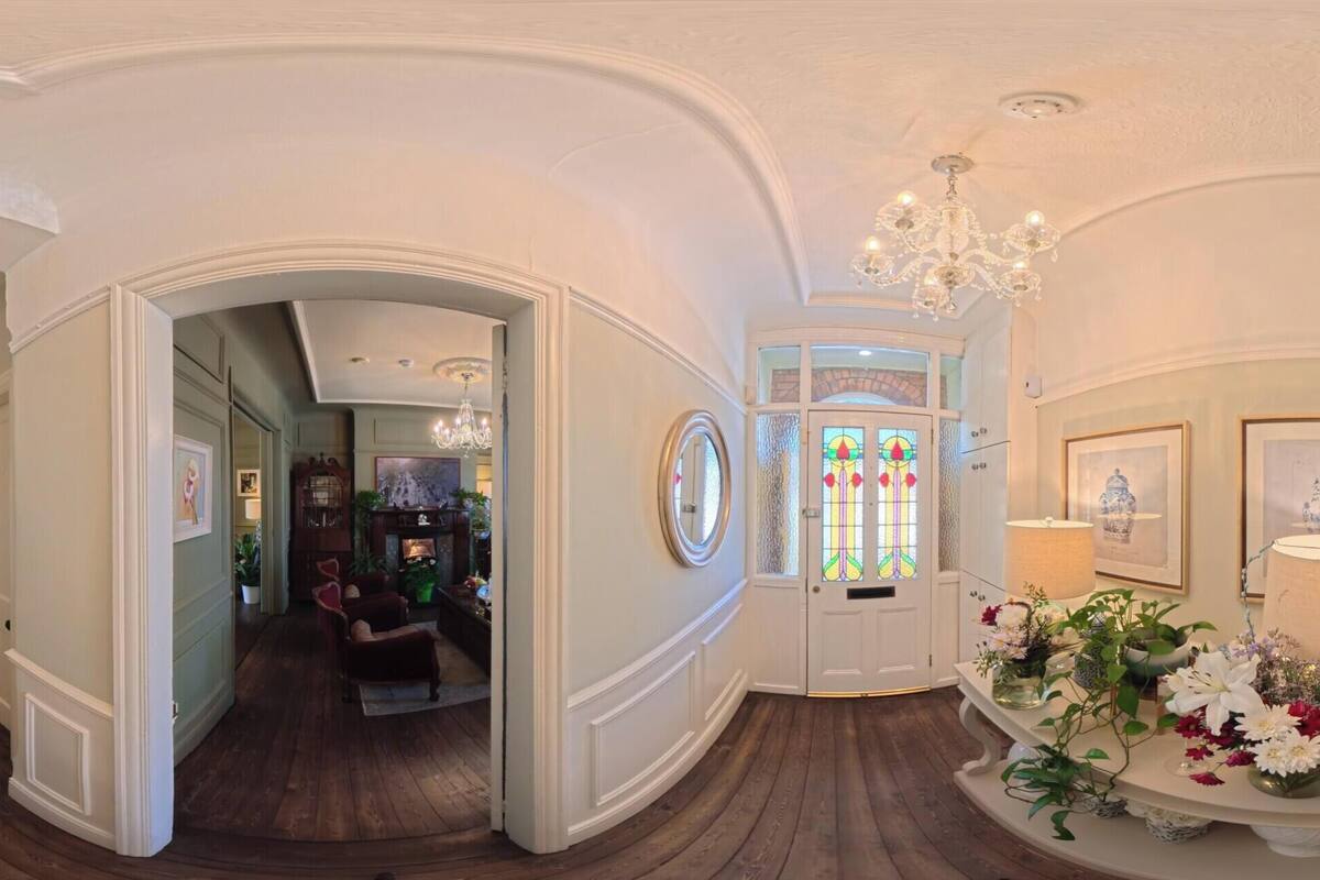 A grand hallway with a staircase, a chandelier, and a door with stained glass.