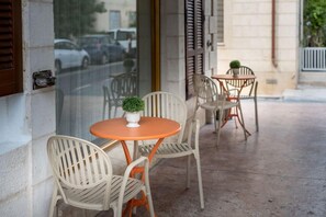 An outdoor seating area with chairs and a table, a small potted plant, and a window with a view of parked cars. - Ness Hotel (Tel Aviv)