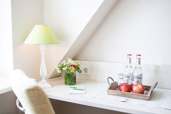 Un bureau bien rangé, avec une lampe, un vase de fleurs, une corbeille de pommes et des bouteilles d’eau.