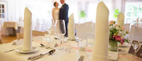 Mesa para recepción de boda con manteles blancos, cristalería y un centro de mesa con velas altas.