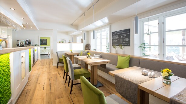 A modern restaurant with wooden flooring, green upholstered chairs, and a bar area with glasses on display. - Paulsen's Landhotel und Restaurant (Bohmstedt)