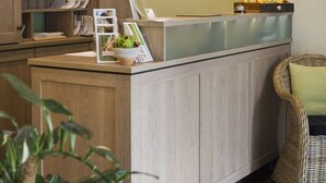 A reception desk with a wooden cabinet, a wicker chair, and a wall-mounted light fixture. - Paulsen's Landhotel und Restaurant (Bohmstedt)