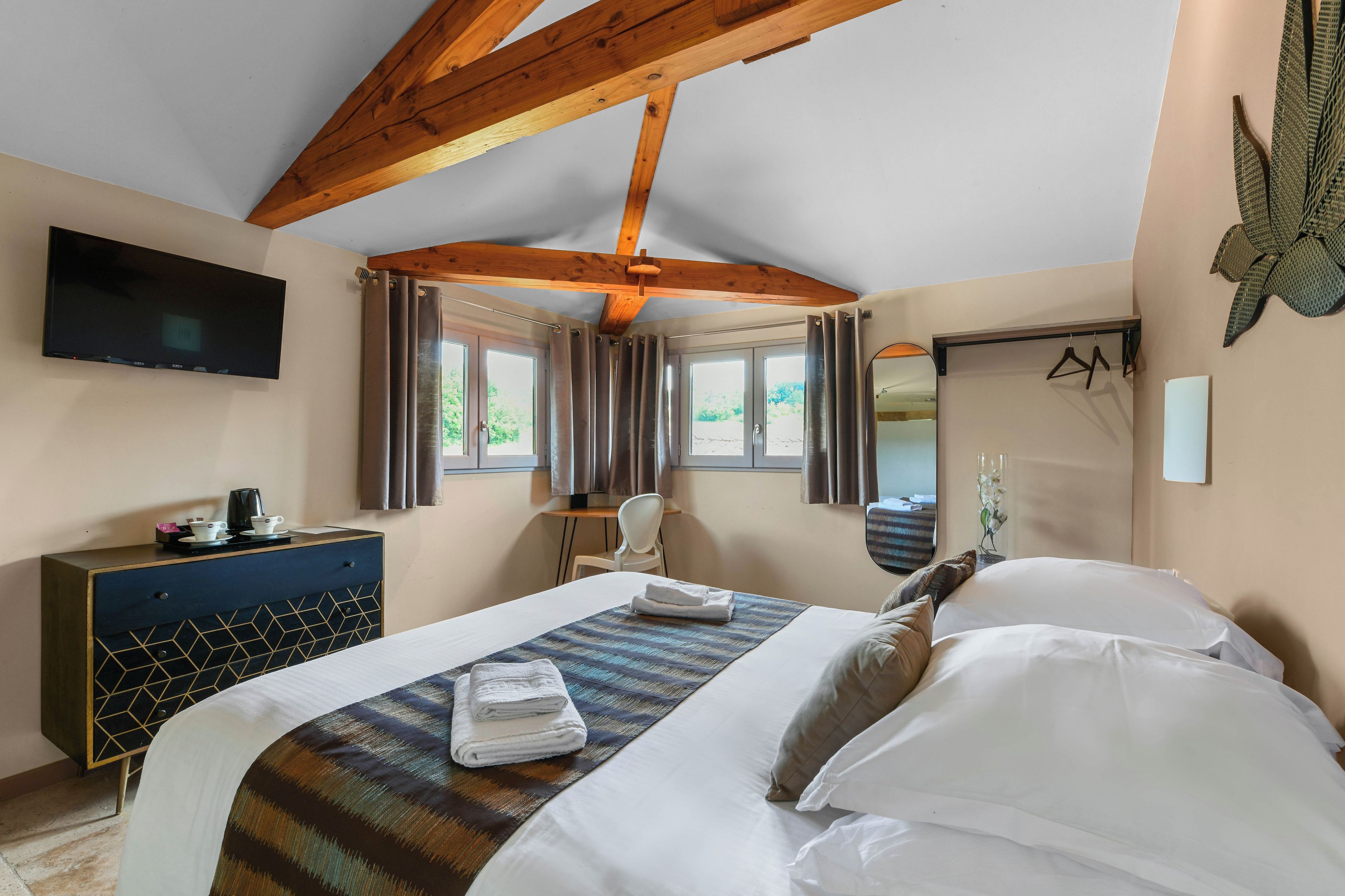 A hotel room with a bed, a desk, a chair, a television, and a window with curtains.