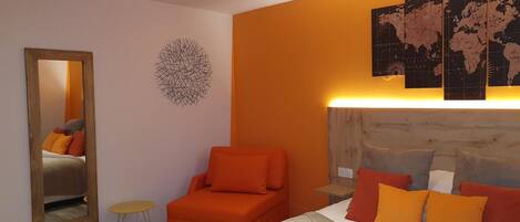 A modern hotel room with a bed, orange armchair, and a large mirror.