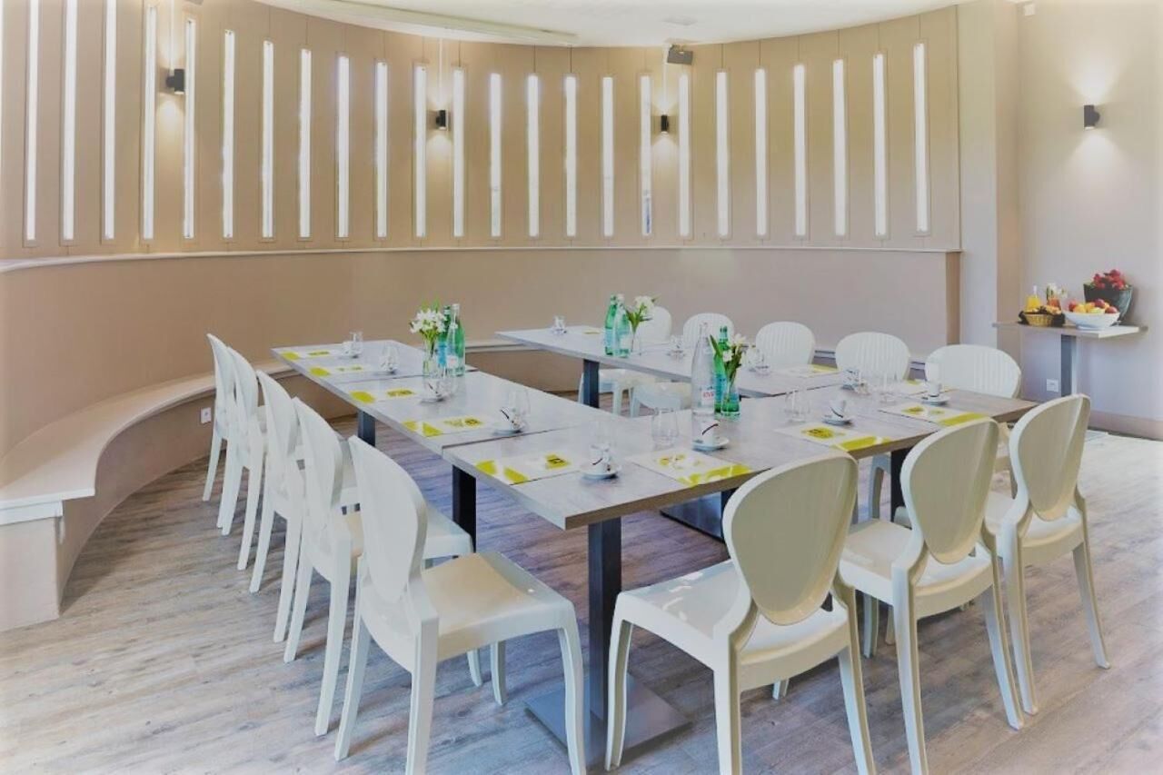 Een vergaderruimte met een lange tafel, witte stoelen en een beige wand met verticale lampen.