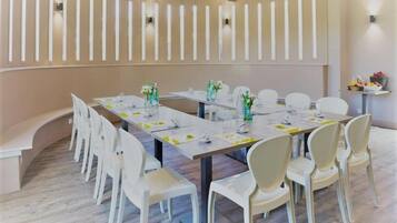 Een vergaderruimte met een lange tafel, witte stoelen en een beige wand met verticale lampen.