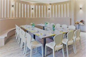 A conference room with a long table, white chairs, and a beige wall with vertical light fixtures. - L'Auberge de Larressingle (Larressingle)