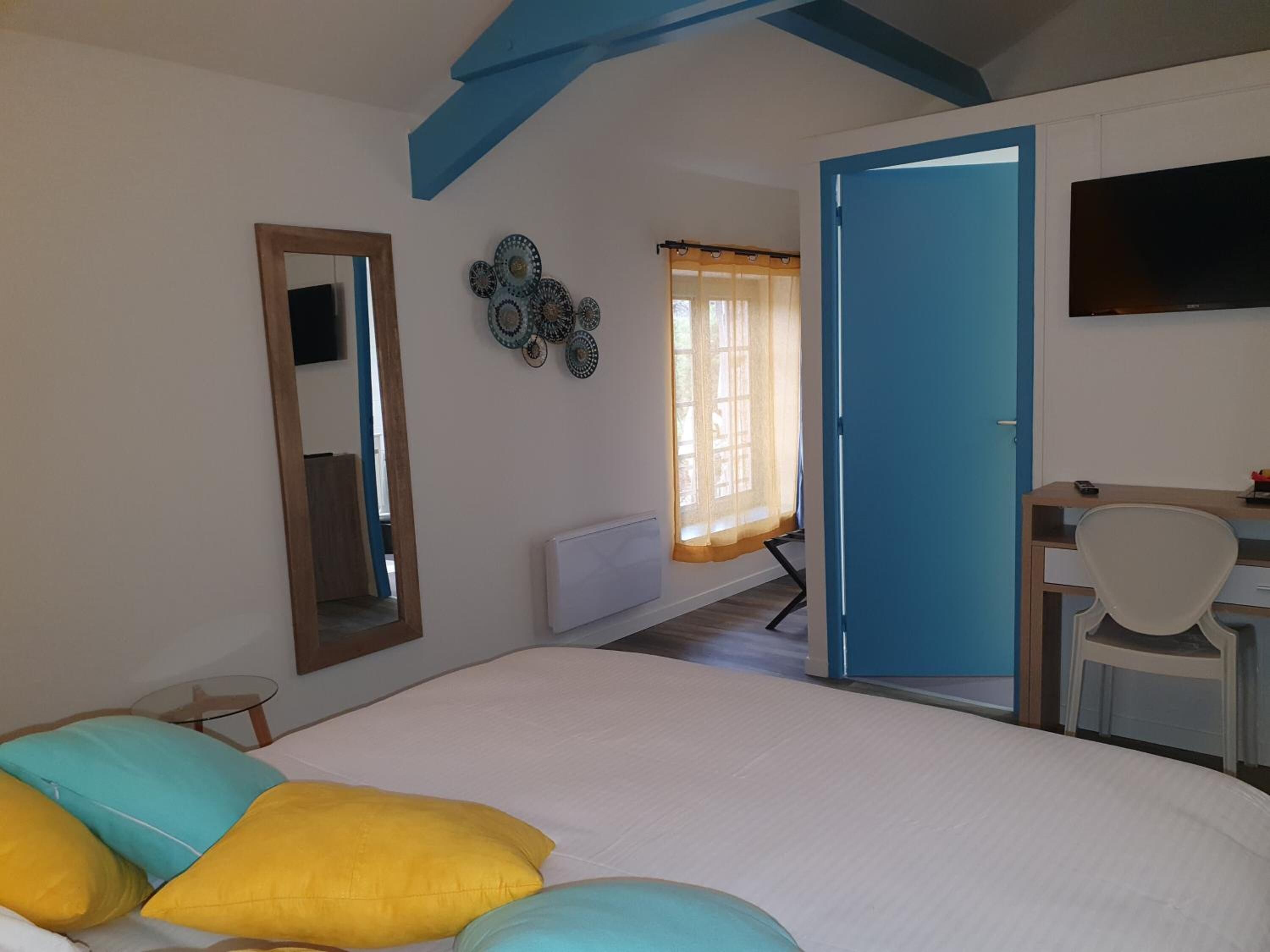 A bedroom with a bed, a desk, a chair, a TV, and a door leading to another room.