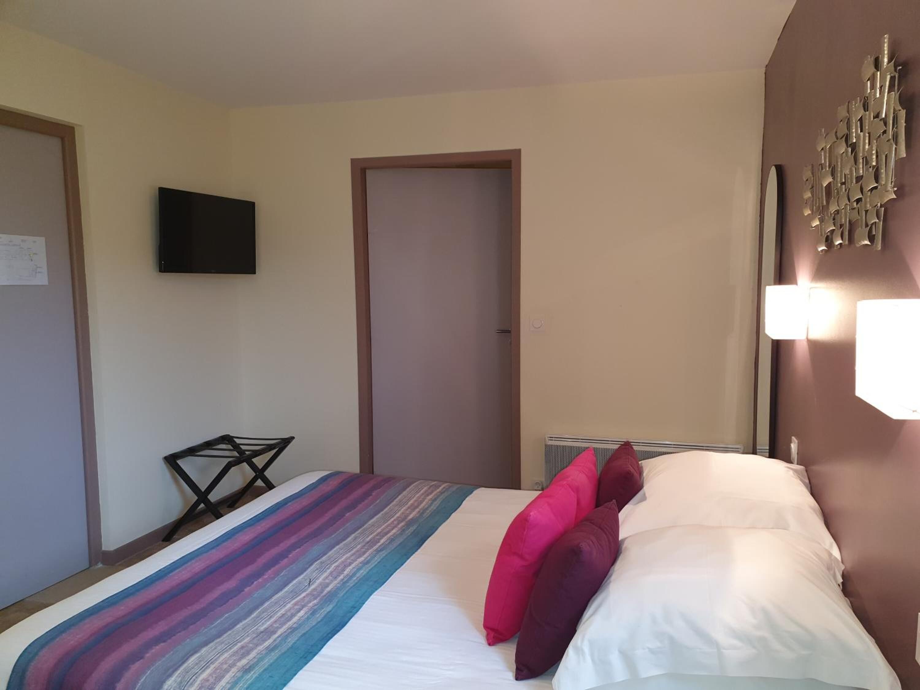 A hotel room with a bed, a flat-screen TV, a door, and a wall-mounted light fixture.