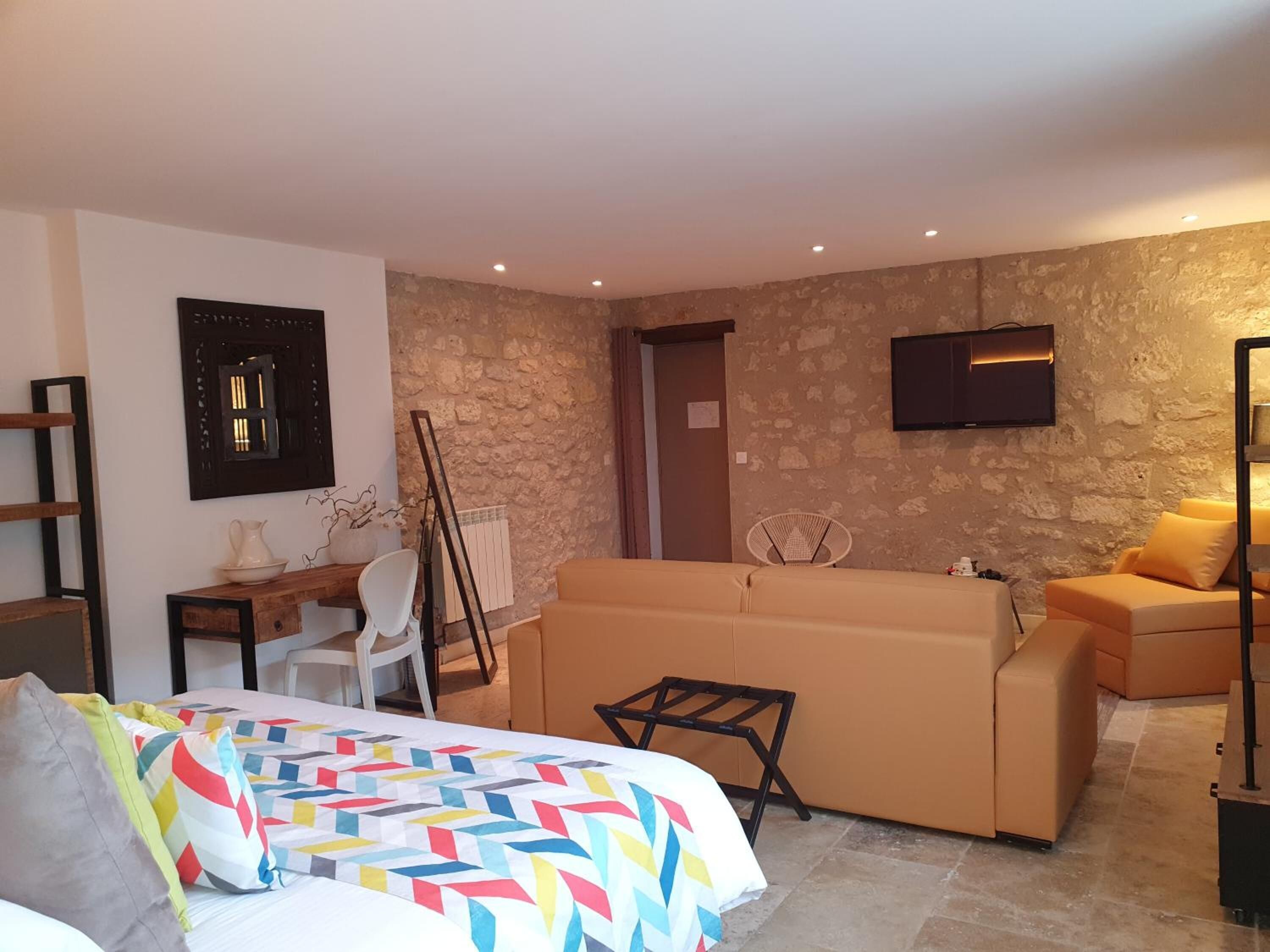 Une chambre d’hôtel moderne avec un lit, un canapé, une télévision et un mur en pierre.