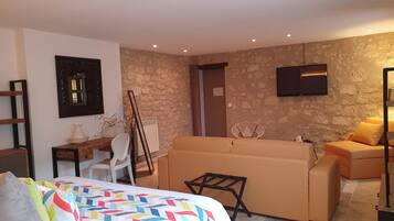 Une chambre d’hôtel moderne avec un lit, un canapé, une télévision et un mur en pierre.