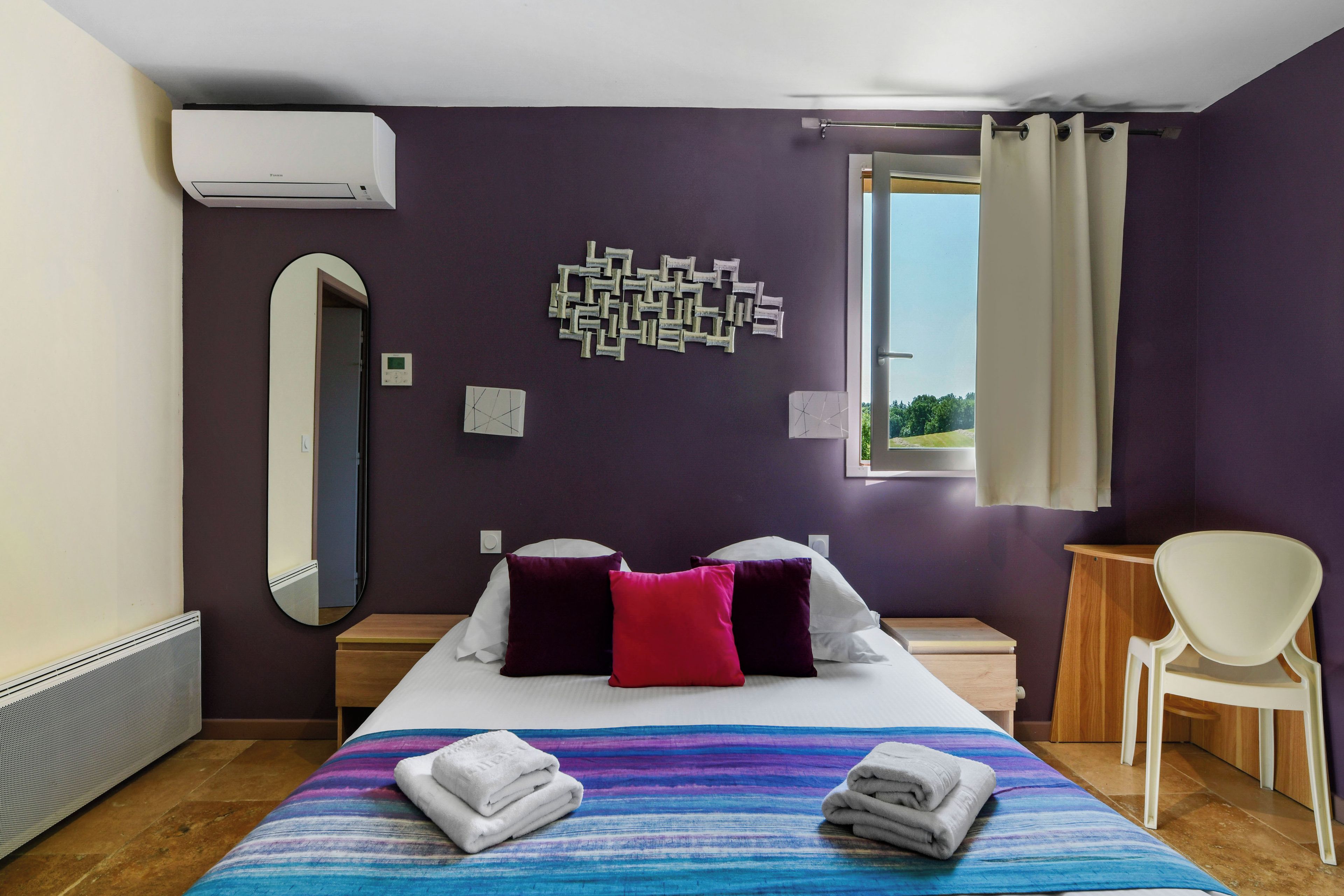 Habitación de hotel con cama, una silla, ventana con cortinas y aire acondicionado instalado en la pared.