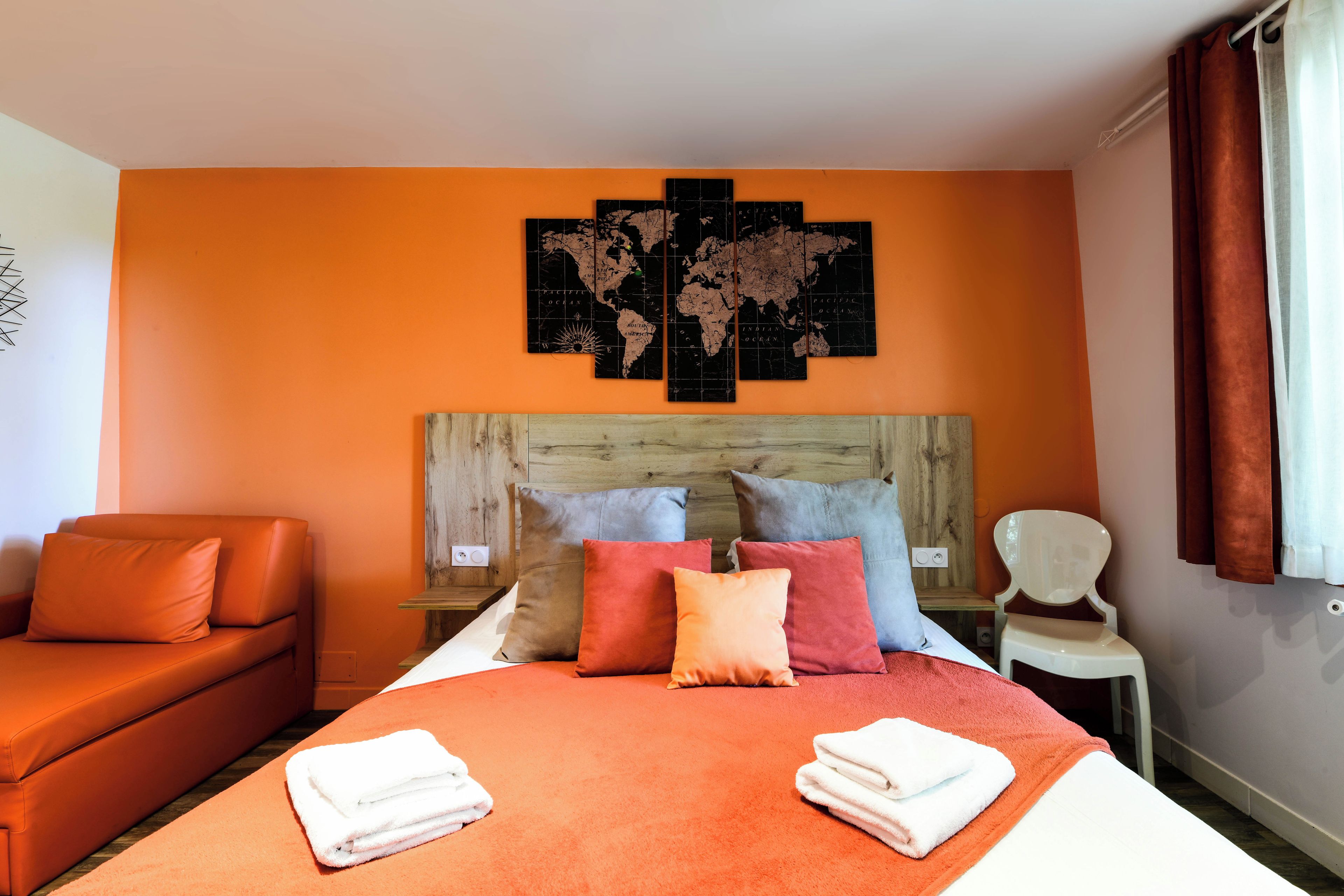 Habitación de hotel con cama, sofá, sillón y un cuadro de un mapa mundial en la pared.