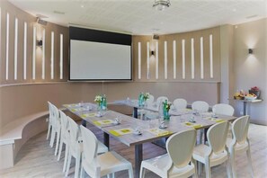 A conference room with a long table, white chairs, a projector screen, and wall-mounted lighting. - L'Auberge de Larressingle (Larressingle)
