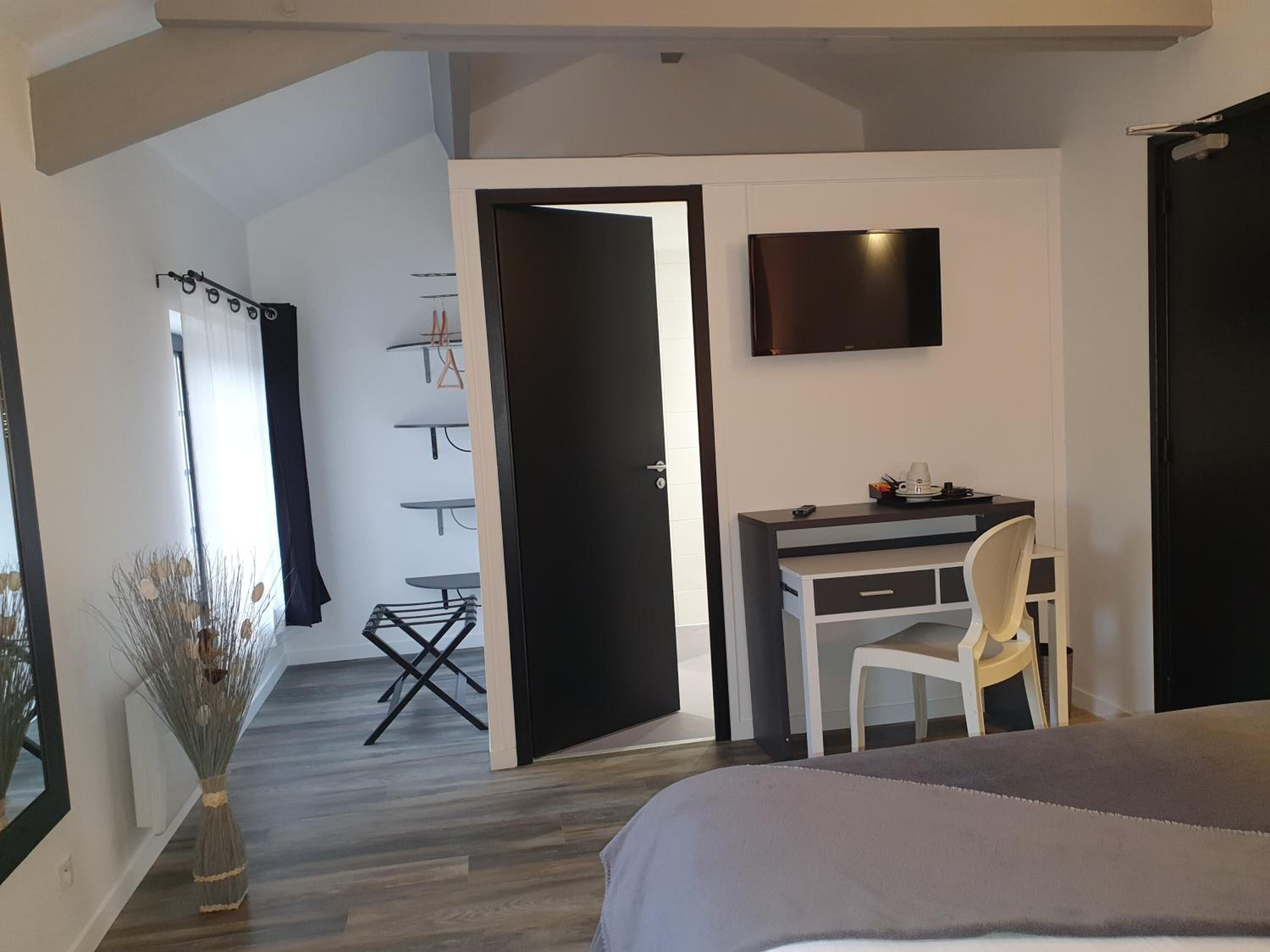 A bedroom with a bed, a desk, and a TV. There is a door leading to a bathroom with a shower and a towel rack.