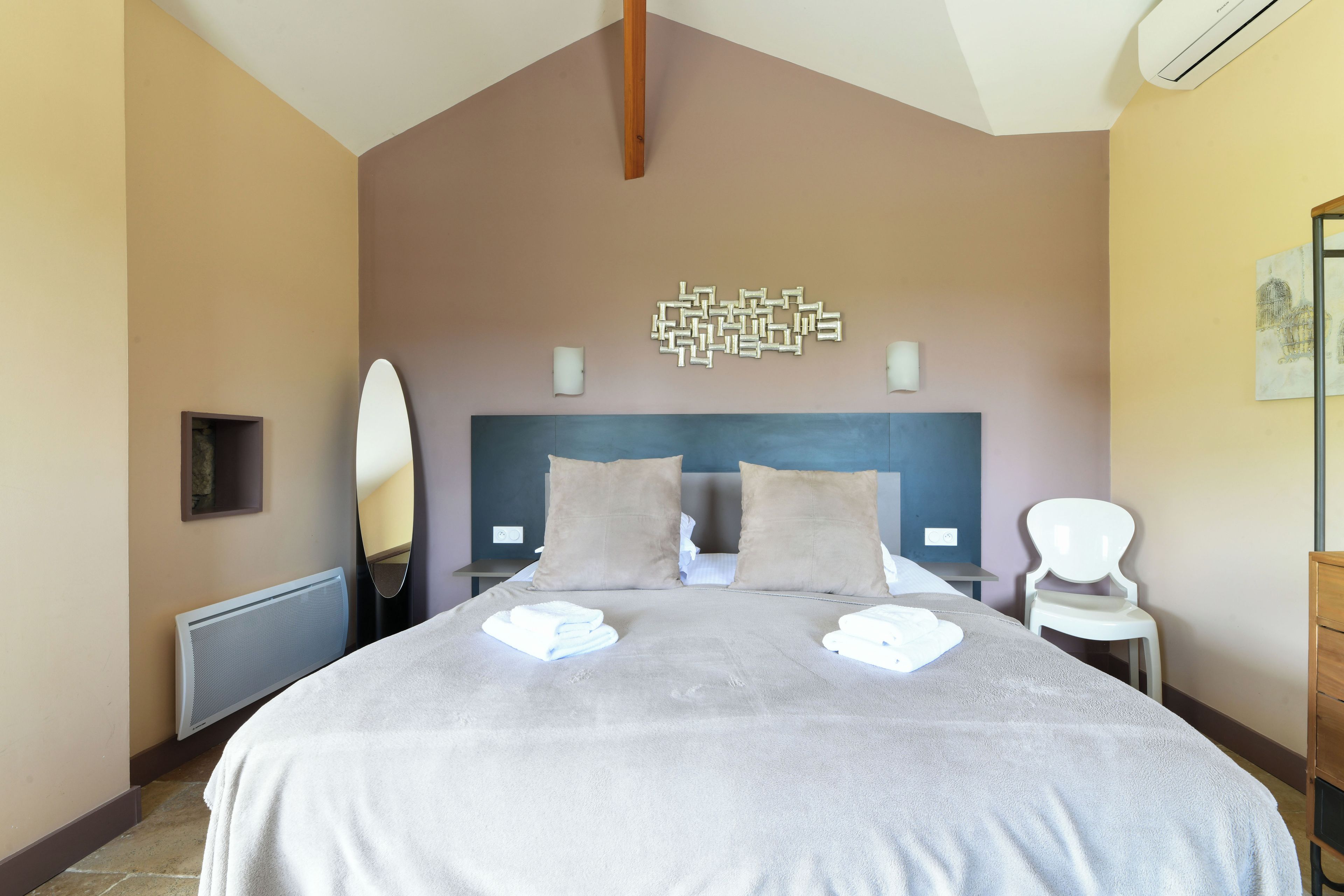 Une chambre d’hôtel avec un grand lit, une tête de lit, deux tables de chevet, un miroir et une œuvre d’art accrochée au mur.