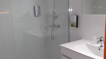 Ein modernes Badezimmer mit einer Glaskabine zur Dusche, einem weißen Waschbecken und einem großen Spiegel.