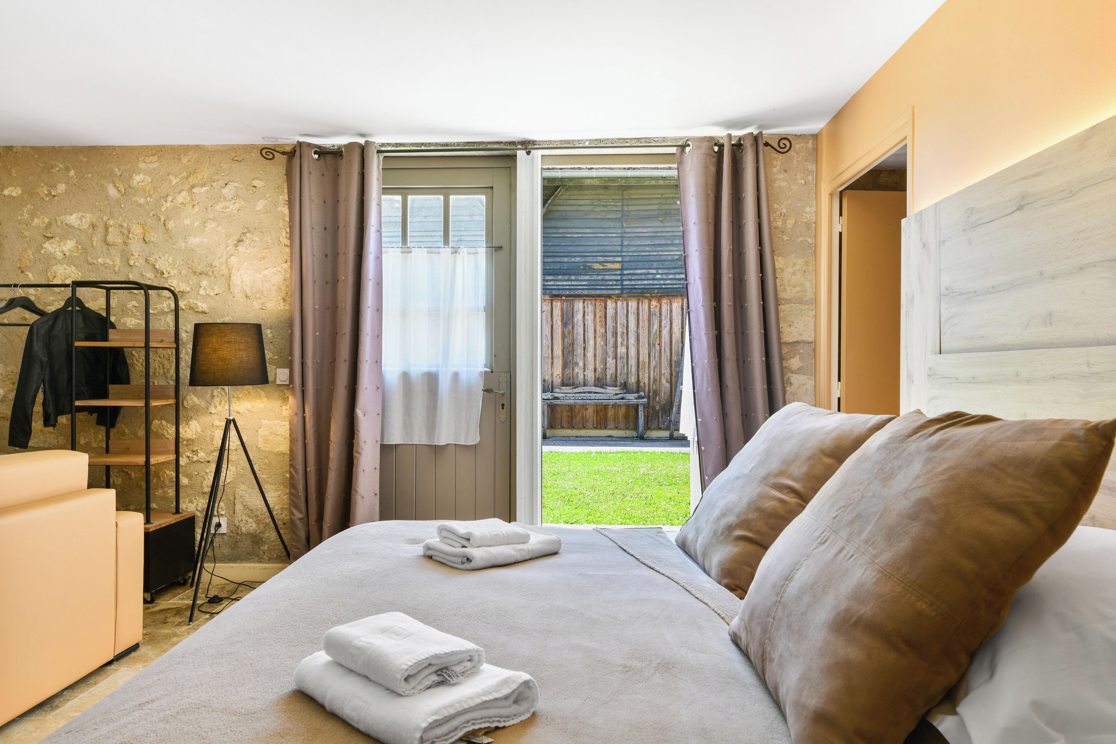 Quarto com cama, mesa de cabeceira, luminária, guarda-roupa e vista para uma área gramada através de uma porta aberta.