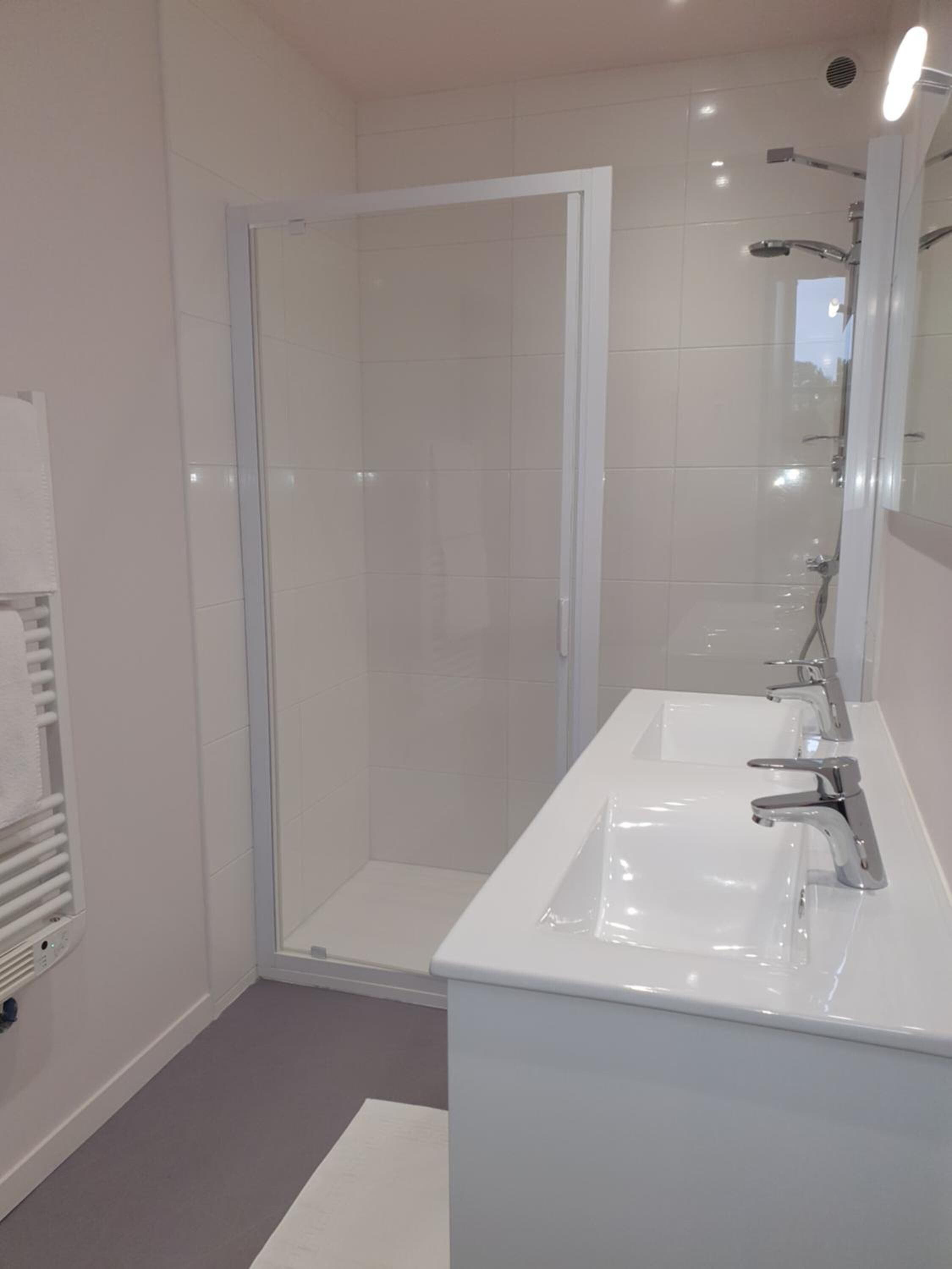 Un baño moderno con cabina de ducha de vidrio, un lavabo blanco con espejo y un perchero para toallas.