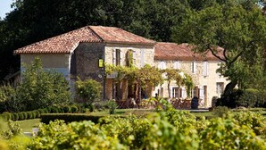 A stone building with a tiled roof, a sign indicating a restaurant, and a well-maintained garden with grapevines. - L'Auberge de Larressingle (Larressingle)