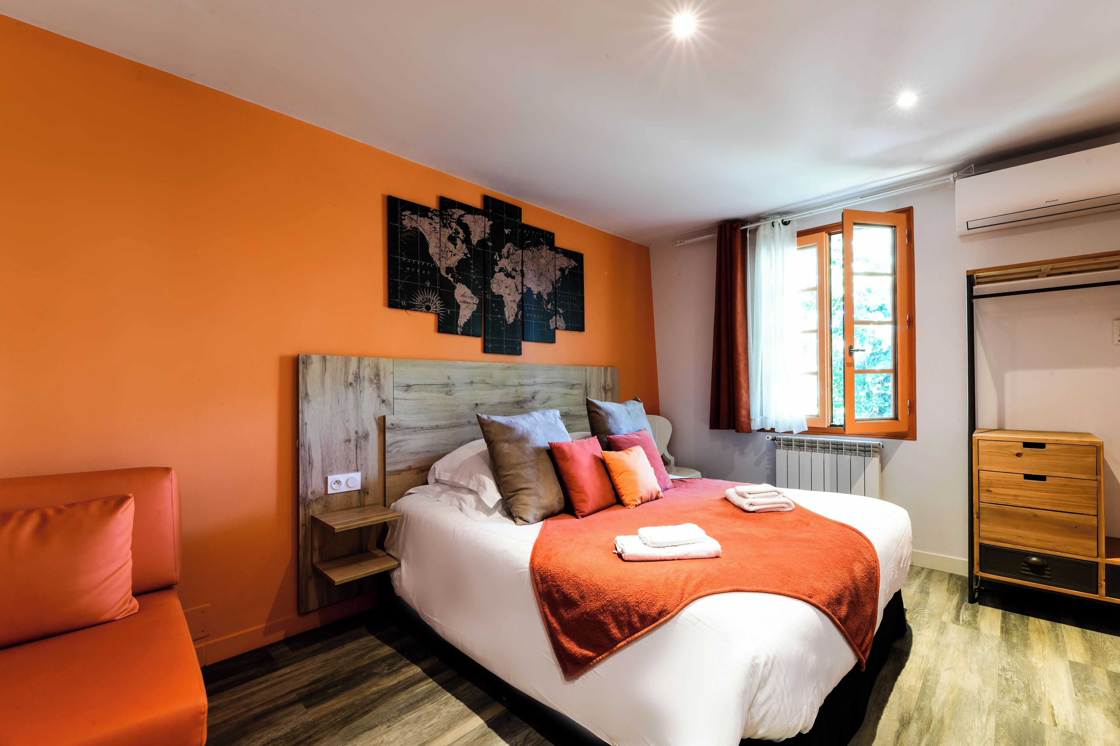 Una habitación de hotel con una cama, cabecero de madera, un mapa mundial en la pared, una ventana con cortinas y un armario de madera.