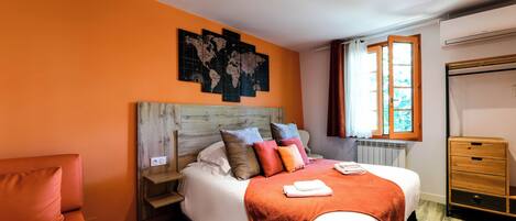 Una habitación de hotel con una cama, cabecero de madera, un mapa mundial en la pared, una ventana con cortinas y un armario de madera.