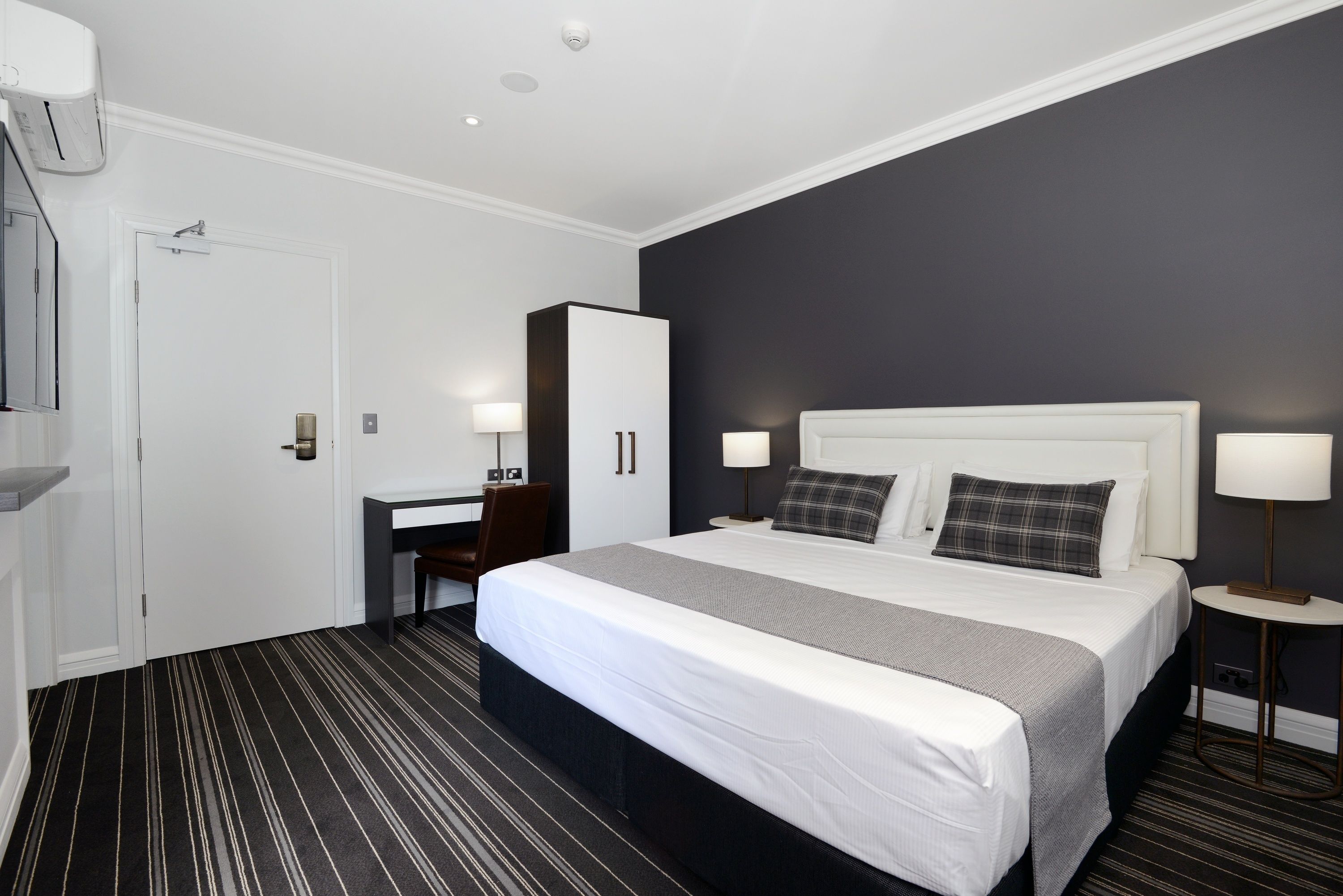 A hotel room with a large bed, a desk, a wardrobe, and two bedside lamps.