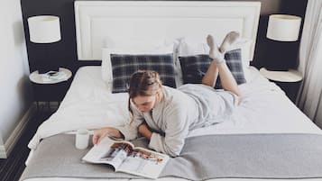 A person lying on a bed with a magazine, a cup, and a pillow.