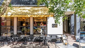 An outdoor café with tables and chairs, a glass storefront, and a sign indicating '6th Street'. - Perouse Randwick by Sydney Lodges (Randwick)
