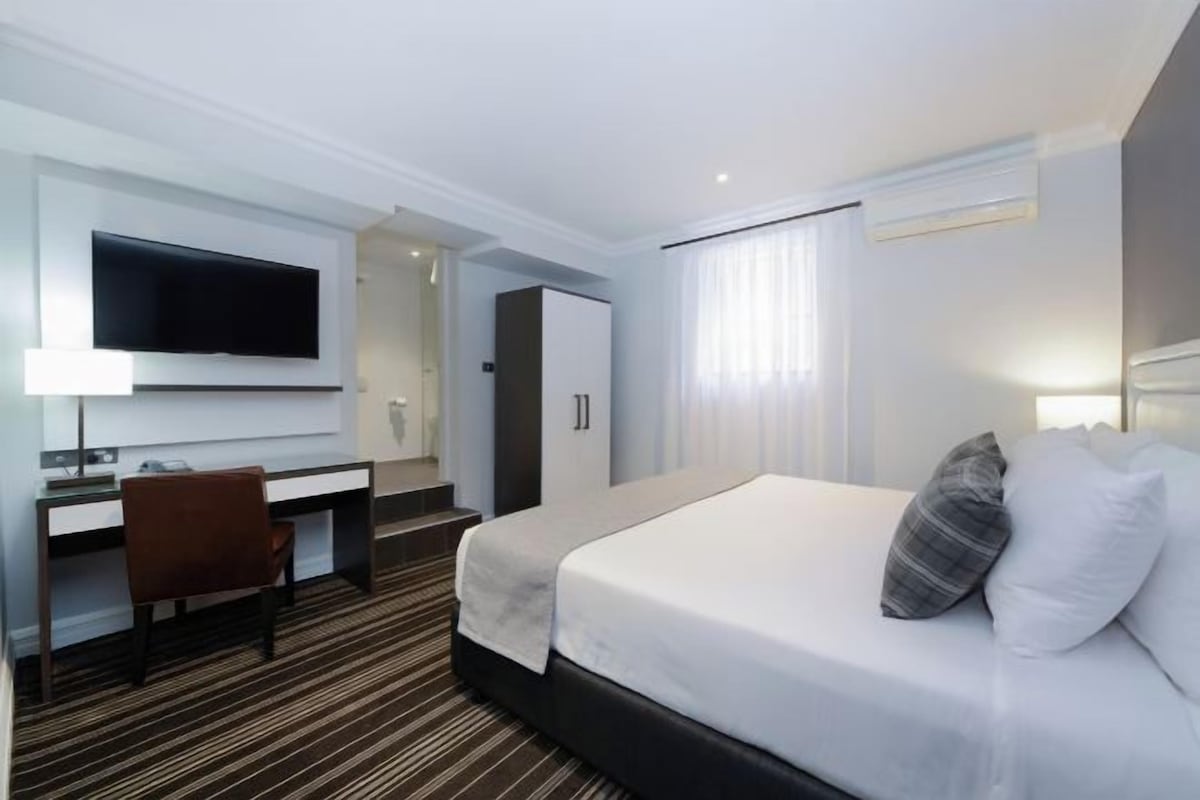 Una habitación de hotel con cama, escritorio, silla, televisor y armario.