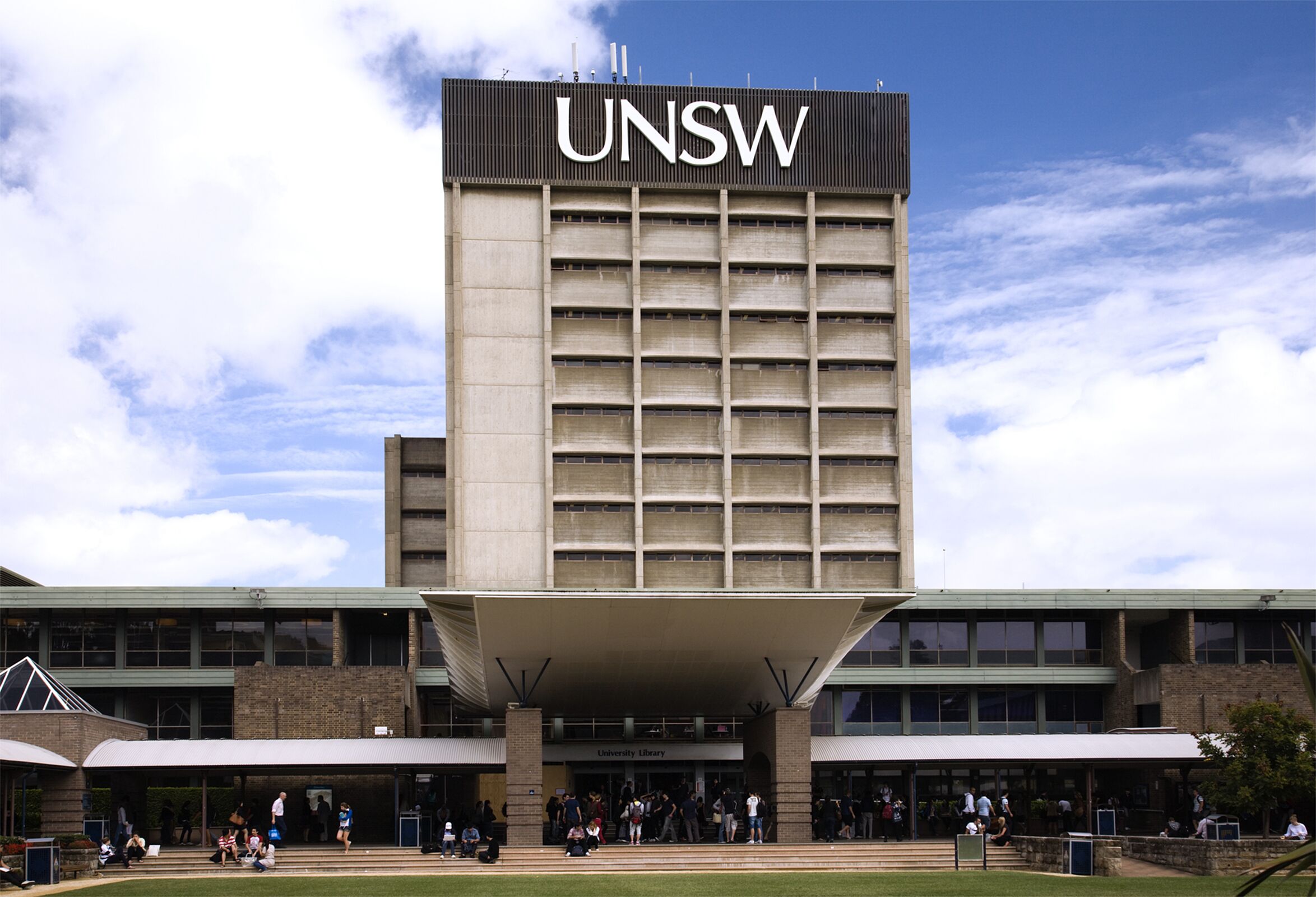 A building with the UNSW logo, a covered entrance, and a grassy area in front.