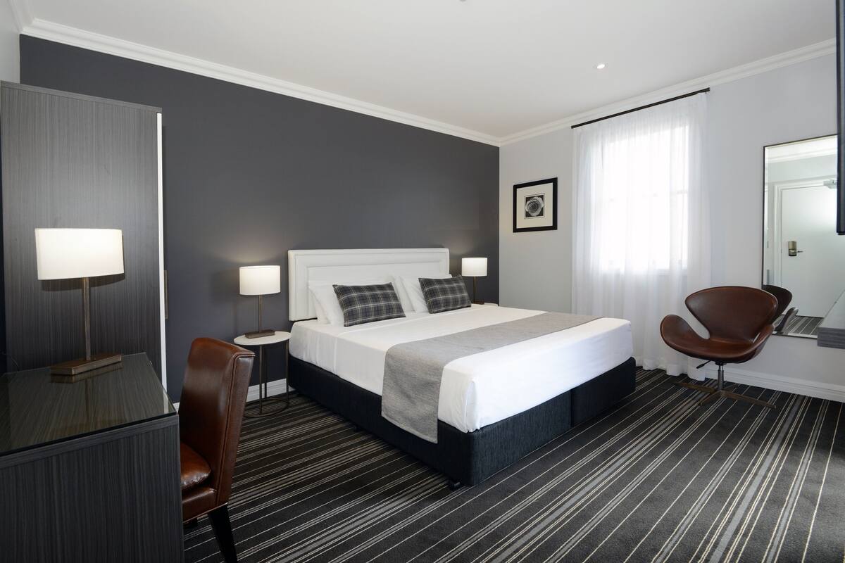 Una habitación de hotel moderna con una cama grande, un escritorio, una silla y un espejo.