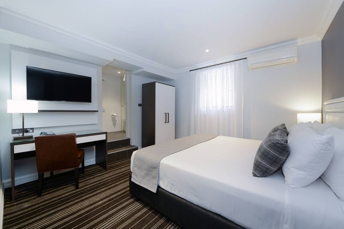 Una habitación de hotel con una cama, un escritorio, una silla, un televisor y un armario.